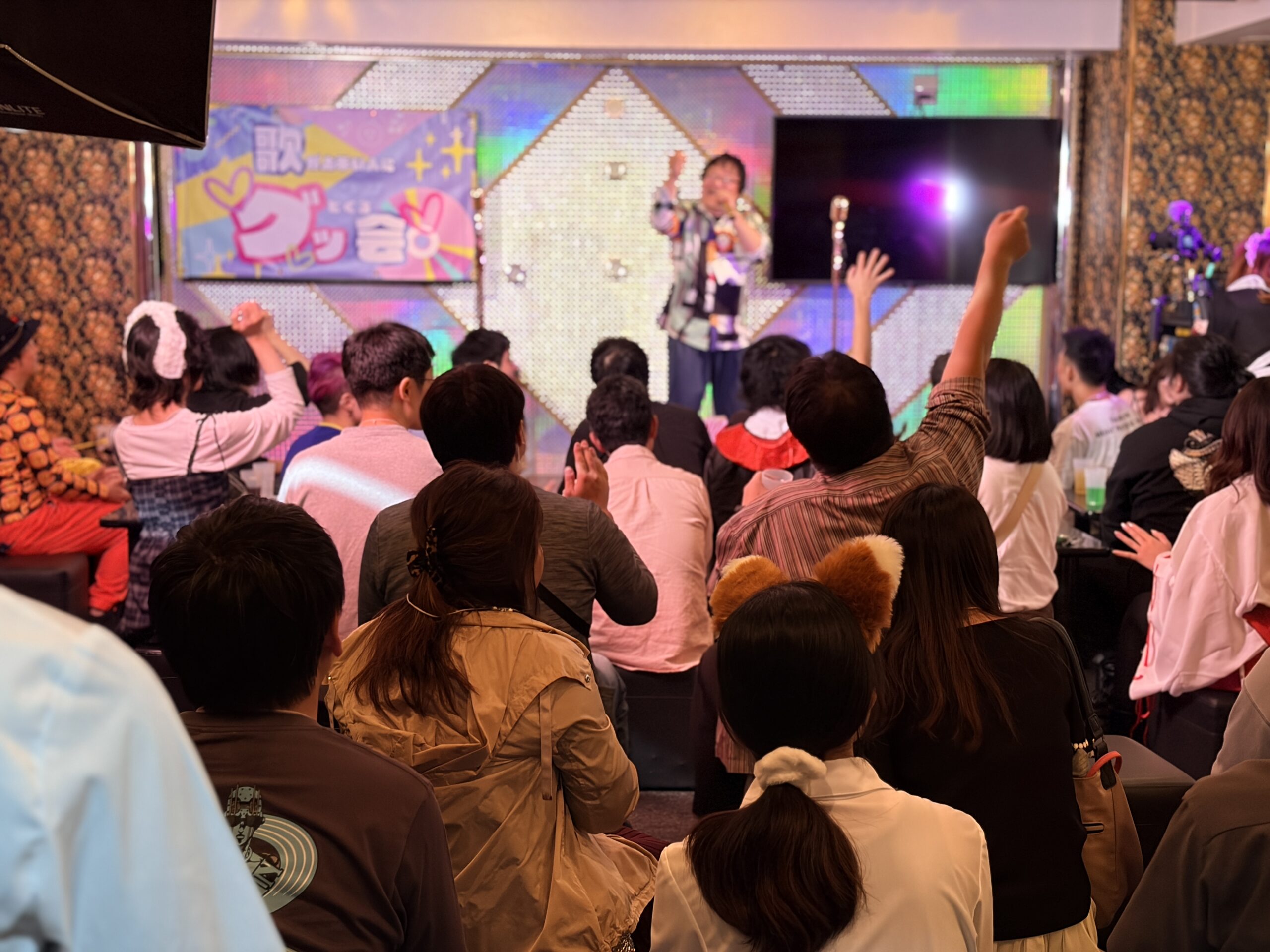 グッ会のステージで歌う出演者に、客席の参加者が手を上げて応える様子